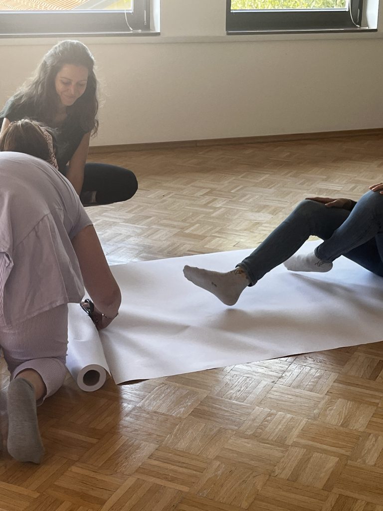 Udeleženki na tla razgrinjata papir za obris telesa